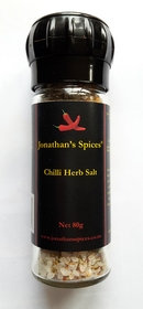 A tall tubular clear glass bottle with a grinder on top and a black yellow and red label containing jonathan's spices chilli rock salt