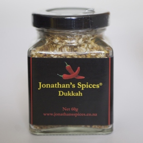A square shaped glass jar with a black, red and yellow label containing Jonathan's Spices dukkah mix