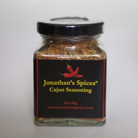 A square shaped glass jar with a black, red and yellow label containing Jonathan's Spices cajun seasoning